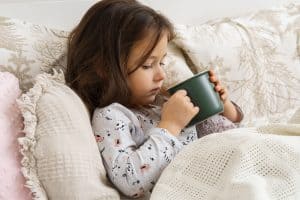 Picture of a sick girl sitting in a bed and holding a mug.