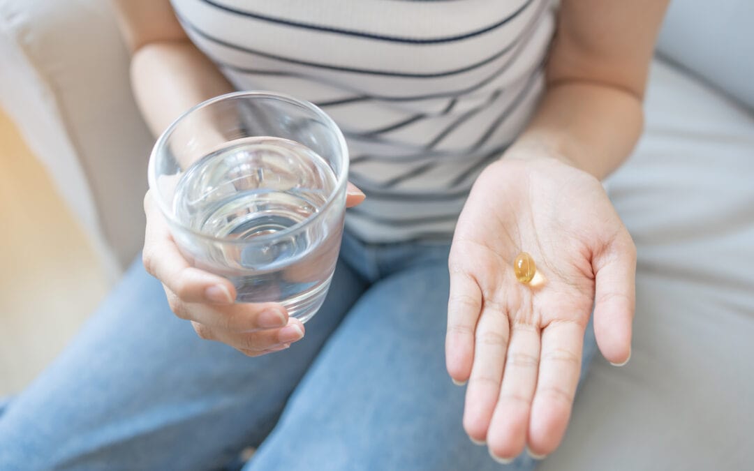 Picture of a woman sitting on a couch and holding a glass of water and a daily multivitamin.